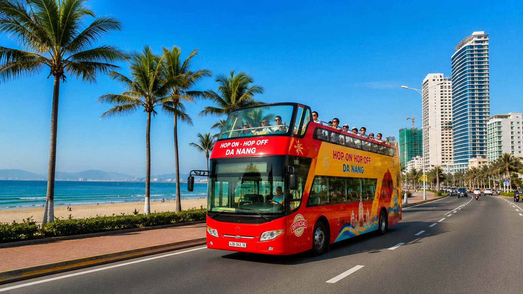 Bright yellow and red hop on hop off da nang double-decker bus driving along My Khe Beach under a clear blue sky