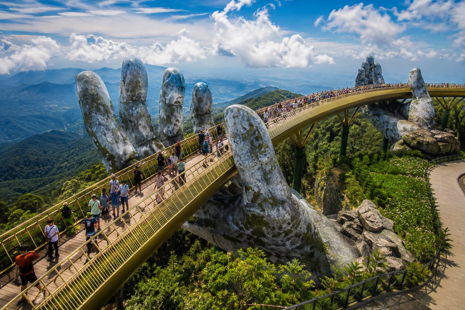 Tourists walking on the famous Golden Bridge held by giant stone hands at Ba Na Hills.