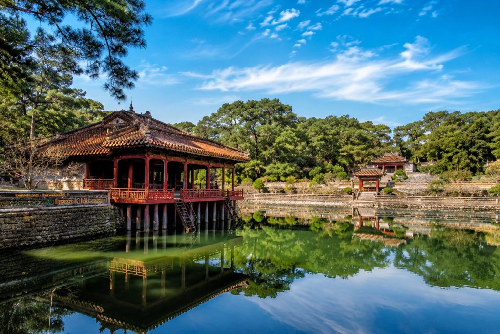 Scenic view of Minh Mang Tomb traditional architecture and tranquil lake.